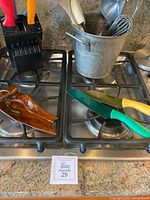 Kitchen knives with colorful handles placed on stove, wooden spoon holder, paper towel holder in background.