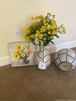 Full view of floral arrangement in ceramic vase, matching ceramic round container, and sunflower-themed wall art on floor against wall