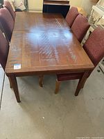 Full view of wooden rectangular dining table with six red upholstered chairs around it.