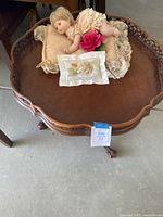 Full view of 26-inch round wooden end table with vintage ceramic doll and decorative pillow on top