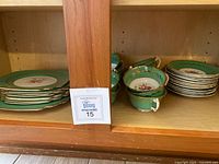 Shelf view showing stacks of green and gold plates on the left and stacked green and gold tea cups on the right
