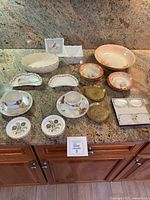 Photo showing multiple porcelain pieces including cups, saucers, bowls, plates, and various decorative items with floral motifs and gold trim.
