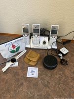 Overview of all items in the lot including the three cordless phones, smartwatch, Alexa Dot, wallet and cords.