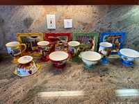 Full group photo of ceramic set pieces on countertop showing plates, mugs, and bowls in colorful themes.