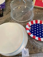 Photo of clear plastic cake cover, white platters, glass platter, and patriotic paper plate on counter.