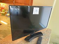 Front view of LG 24-inch television with screen and stand visible, remote control placed beside it.