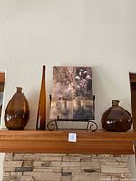 Photo showing three brown vases and floral canvas art on black metal stand on a wooden mantle.