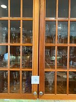Crystal stemware displayed inside a wooden glass cabinet, showing rows of various wine glasses, goblets, and flutes.