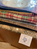 Close view of stacked placemats including woven and plaid patterns with package of white paper doilies on top.