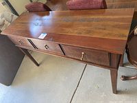Full view of wooden sideboard showing front with three drawers and tapered legs.