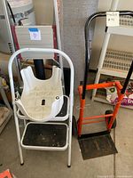 Photo of three step stools and an orange-handled dolly standing upright.