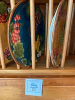 Eight Susan Wingers decorative ceramic plates with fruit motifs displayed in a wooden plate rack