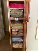 Open wooden cabinet with six shelves showing folded towels and blankets in various colors and textures.