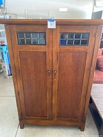 Front view of wooden TV armoire cabinet showing double doors with patterned glass inserts.