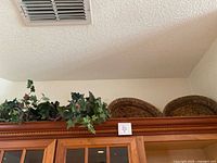 Two large woven round baskets and faux ivy plants on top of wooden kitchen cabinet against a white wall and ceiling.