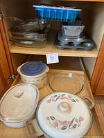Shelved cabinet with various bakeware items including glass baking dishes, metal muffin pan, and foil pans