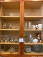 Full view of cupboard shelves containing various glassware and bowls including glasses, mugs, and plates.