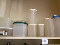 Several translucent plastic kitchen containers of various sizes with different colored lids on a shelf.