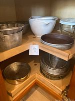 Corner shelf displaying white plastic mixing bowls, a round metal tub, and a metal pie pan on top shelf; metal wire baskets, glass plates, and baskets on lower shelf.