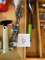 Close-up image showing manual hand mixers with wooden handles, a Microplane grater, and a corkscrew in a wooden drawer organizer.