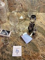 Clear glass decanter, wine glasses, cocktail shaker, drink stirrers, pourers, and small bar tools displayed on countertop.