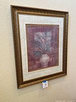 Front view of the framed picture showing vase with leafy plant artwork and ornate gold frame