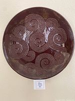 Front view of round decorative wall plate showing raised spiral dot pattern in brown glossy finish