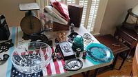 Wide shot showing patriotic cast iron decor, vintage scale, glass bowl, blue glass plate, small metal decorative items, wooden box, and vintage medical apparatus arranged on table with American flag underlay.