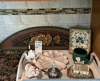 Photo of assorted Irish-themed decorative and kitchenware items on a table including a wooden decorative sign, ceramic mug, porcelain cream pitcher, ceramic serving dish, and shamrock plaque.