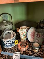 Shelf with assorted vintage pottery and stoneware items including German beer stein, ceramic salt container, painted pitcher, decorative plates, and small pottery cups.