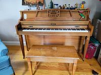 Front view of Baldwin upright piano with matching bench showing minor wear and music books on top.