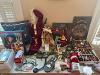 Full assortment of Christmas and Santa themed decorations displayed on a table including pillows, figurines, metal decorations and signs.