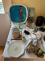 Overview of lot items on table including ceramic plate, duck figurine, glass starfish dish, metal lantern with wicker, painted tray, and several nautical décor pieces