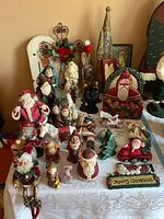Top-down view of assortment of Christmas figurines and decorations on a white tablecloth, featuring Santa Claus figurines, Christmas trees, wreath, and assorted holiday decor