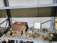 Shelf with various vintage and antique brass and metal collectibles including plaques, keys, ornate brass pieces, and a wooden box with brass handle.