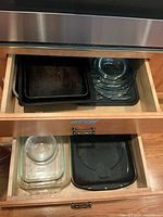 Drawer with stacked clear glass bakeware dishes and black metal pans including a rectangular grill pan with ridges marked 'GRILL PAN'