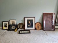 Wide shot of all framed pieces arranged on carpet floor, including portraits, needlework, and collage frame.