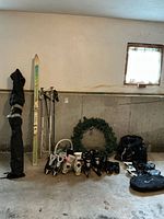 Wide view showing all winter sports gear against wall including skis, poles, boots, skates, snowshoes and bags.