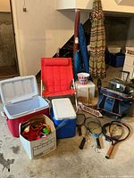 Photo showing the large red Rubbermaid cooler open, medium blue Igloo cooler, small white Coleman cooler, red folding chair with white metal frame, basket, and assorted items in a box.