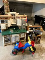 Photo of Step2 plastic play kitchen, wooden dollhouse with furniture, and blue plastic ride-on tricycle