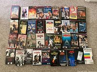 Photo showing 38 VHS tapes laid out on carpet, featuring a wide variety of classic movies, dramas, comedies, musicals, and sports tapes.