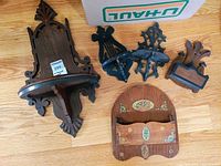 Five wooden wall decorative pieces placed on wooden floor; 2 shelves and 3 sconces with vintage carved details and some floral painting on one shelf.