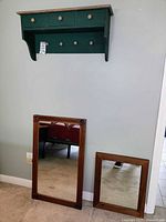 Wall shelf mounted on the wall above two wooden framed vintage mirrors leaning against the wall on carpeted floor.