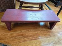 Rectangular red wooden footstool showing surface wear and simple design.