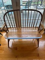 Front view of the Windsor style oak wooden bench showing the spindle backrest, natural wood grain seat, curved armrests, and four legs.