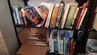 Shelf with multiple books including technical, novels, and reference books in various binding formats, showing a packed box of books below.