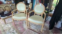 Pair of two French provincial style armchairs with pale green peau de soie fabric upholstery and carved wooden frames on a floral-patterned rug.