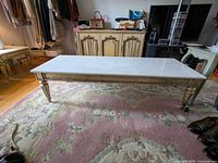 Side angle view of coffee table showing marble top and gilded carved wood legs.