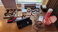 Costume jewelry assortment displayed on window sill including black beaded necklaces, clip earrings, multi-colored bracelets, rings, and a pink jewelry case