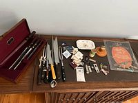 Full display of all items laid out on wooden dresser including cutlery, carving guide, cigar cutters, matches, small plates and other accessories